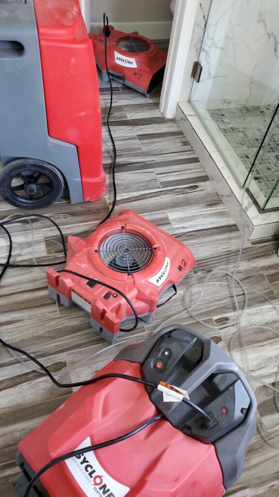 Air mover and dehumidifier drying a floor next to a glass shower