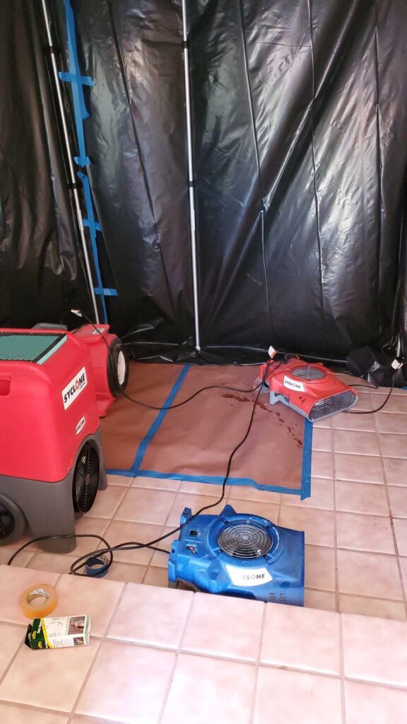 Dehumidifier and air mover inside black plastic containment
