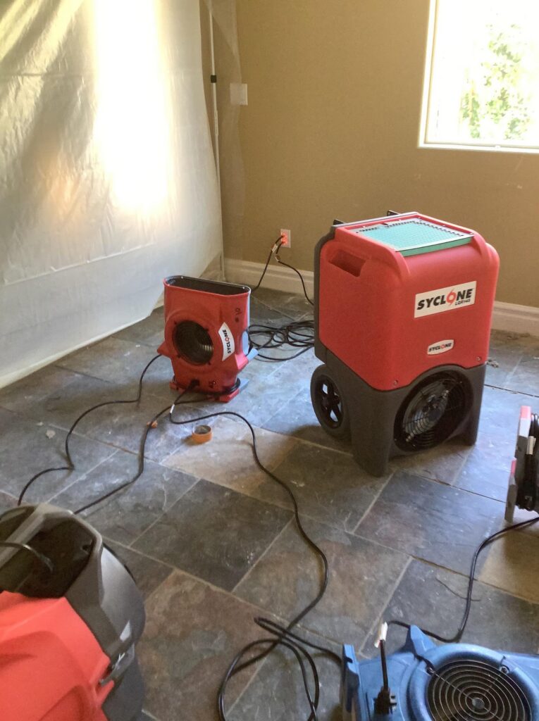 Dehumidifier and air mover drying a room with containment along one wall