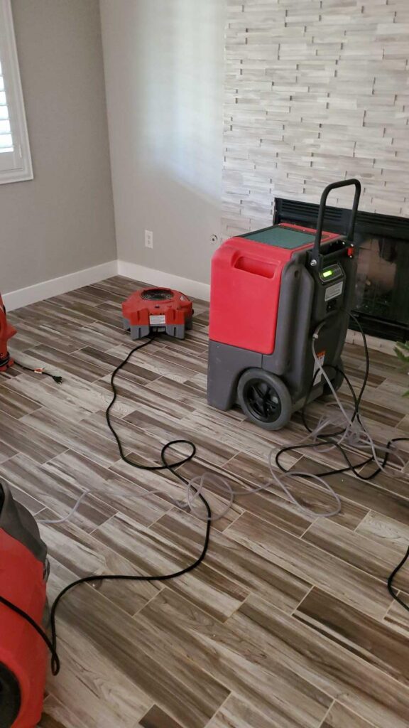 Dehumidifier and air mover drying a living room with wood-look tile floor