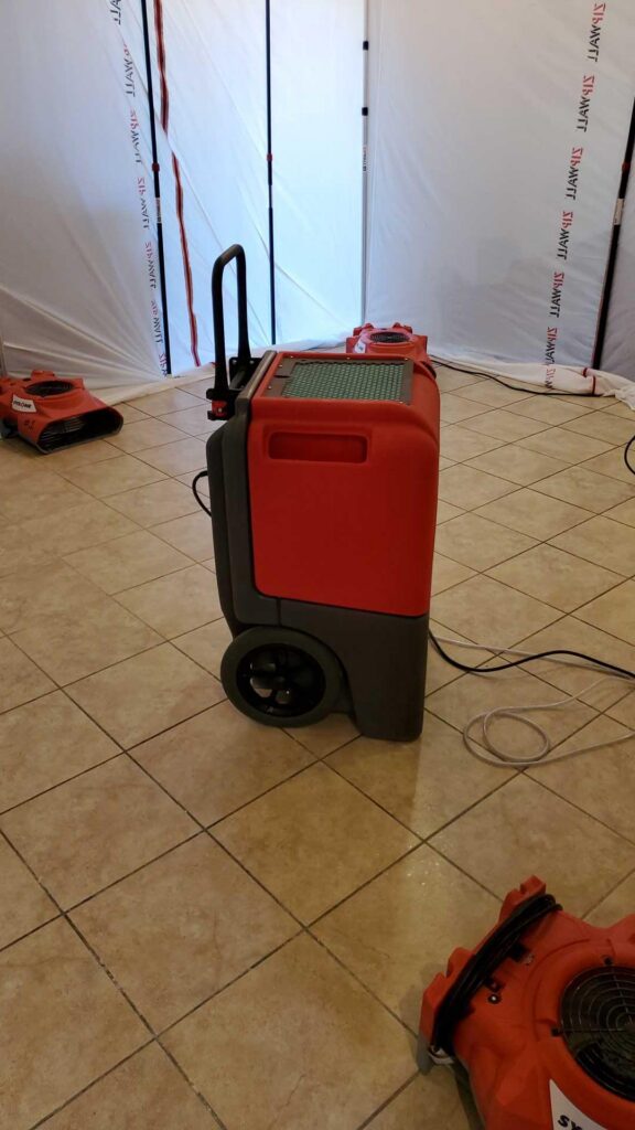 Dehumidifier and air mover running inside plastic containment on a tile floor